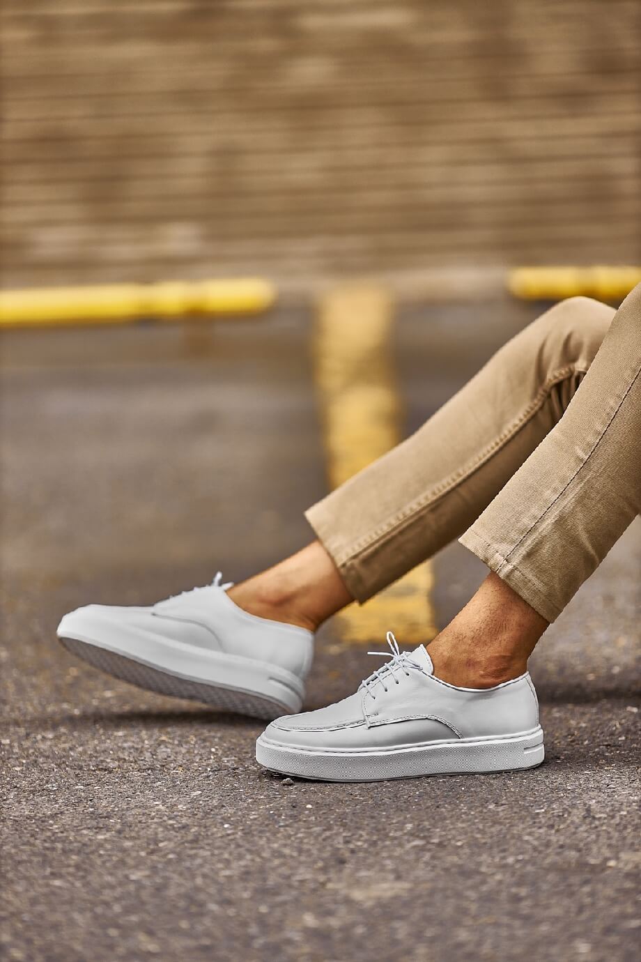 White leather lace-up casual derby shoes worn with beige chinos, photographed outdoors on a city street.