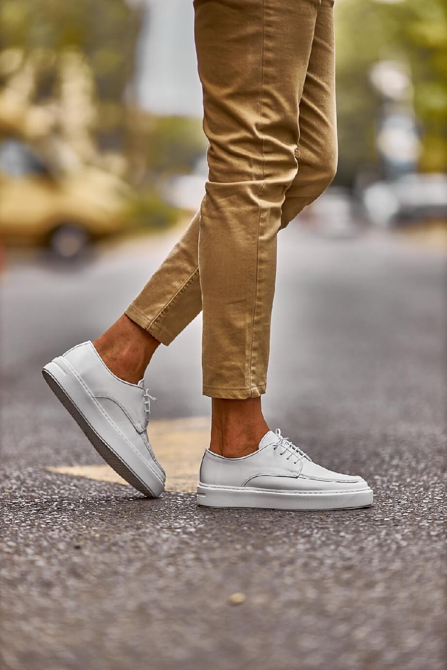White leather lace-up casual derby shoes worn with beige chinos, photographed outdoors on a city street.