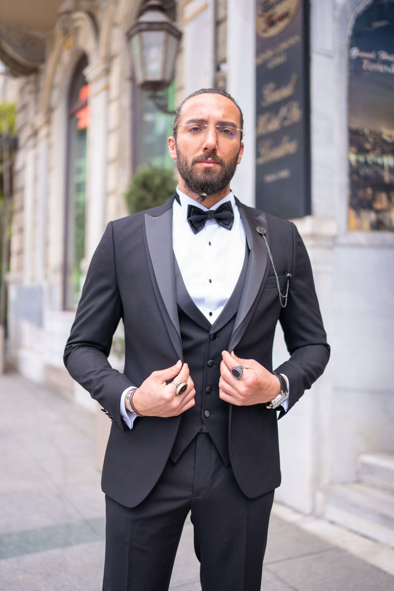 Black satin-collar men’s tuxedo in slim fit, styled with a vest, bow tie, and formal pants – a 5-piece formal set ideal for weddings, galas, and luxury events.