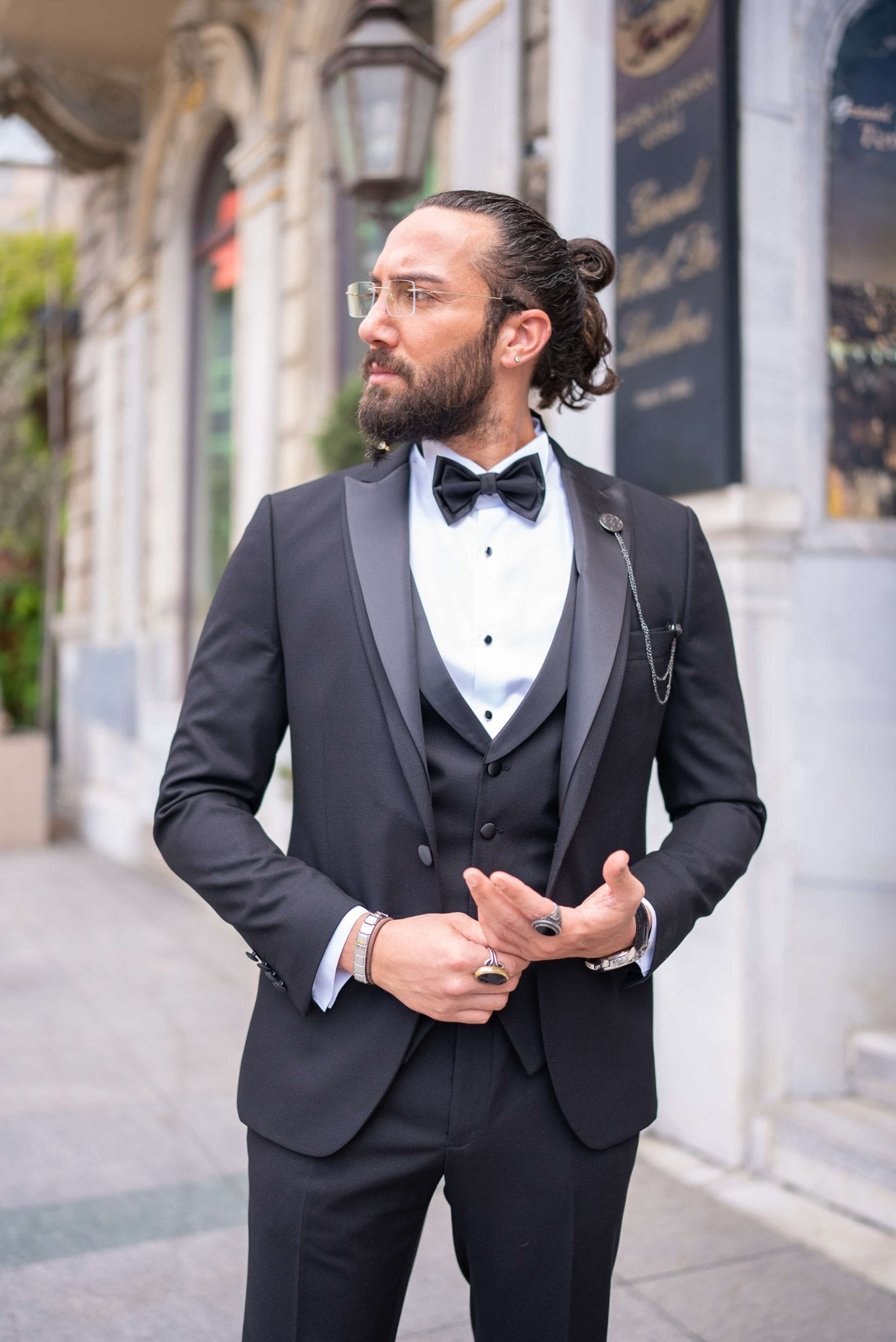 Black satin-collar men’s tuxedo in slim fit, styled with a vest, bow tie, and formal pants – a 5-piece formal set ideal for weddings, galas, and luxury events.