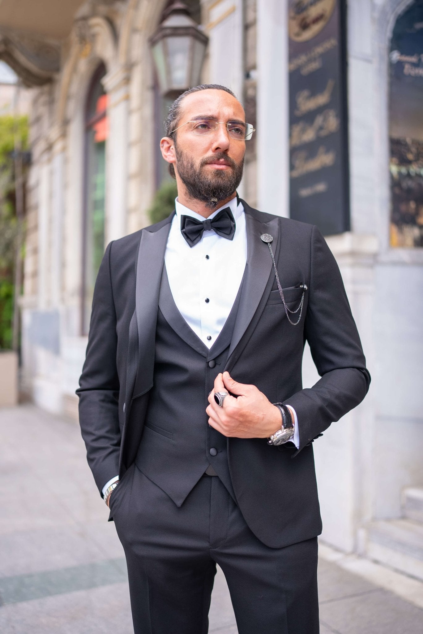 Black satin-collar men’s tuxedo in slim fit, styled with a vest, bow tie, and formal pants – a 5-piece formal set ideal for weddings, galas, and luxury events.