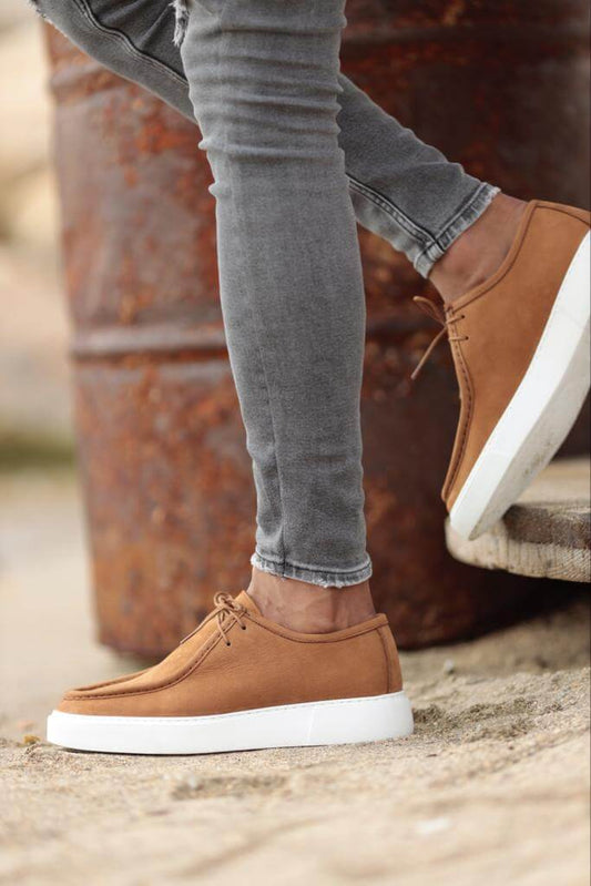 camel suede casual derby shoes with white EVA soles, worn with grey ripped skinny jeans, styled in an outdoor setting against a rusted barrel.