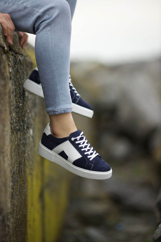 Navy and white leather sneakers on feet, styled by the waterfront. 