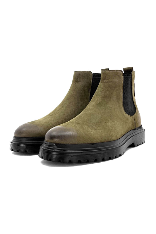 A pair of khaki green Chelsea boots in nubuck leather with thick black EVA soles and black elastic side panels, photographed from both a side-angle and a dynamic lifted view.